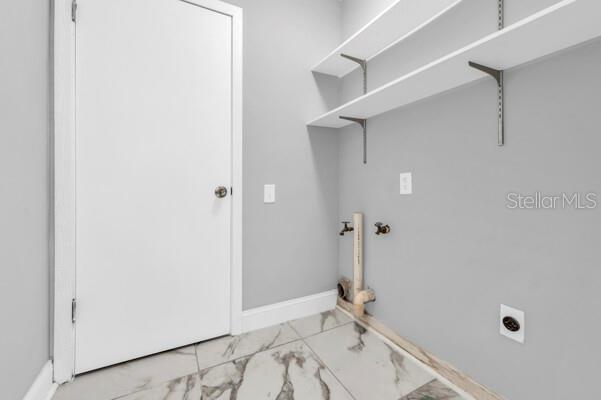 A laundry room with white walls, marble-look tile flooring, open shelving, and utility hookups — 1502 NE BUCKEYE ROAD NE UNIT 2, WINTER HAVEN, FL