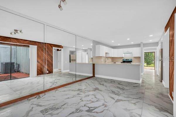 A room with marble-look tile flooring, a mirrored wall, and an open kitchen with white cabinets — 1502 NE BUCKEYE ROAD NE UNIT 2, WINTER HAVEN, FL