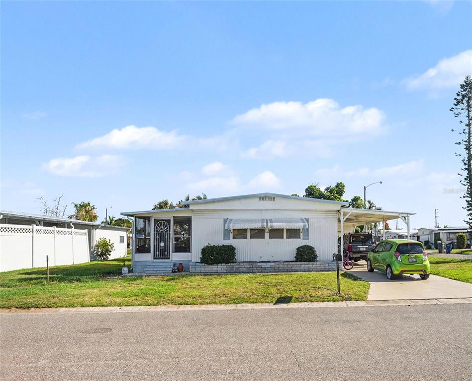 A single-story mobile home with a carport and a green car parked in front — 309 50TH AVENUE TERRACE E, BRADENTON, FL