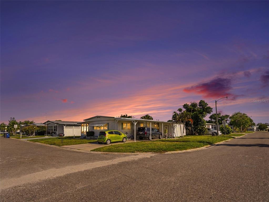A single-story manufactured home with a carport sits on a corner lot at sunset — 309 50TH AVENUE TERRACE E, BRADENTON, FL