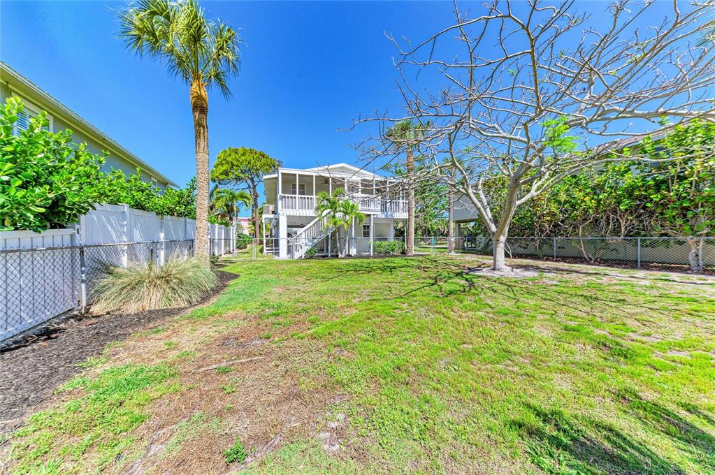 A two-story house with a screened porch stands behind a fenced grassy backyard — 517 SPRING AVENUE, ANNA MARIA, FL