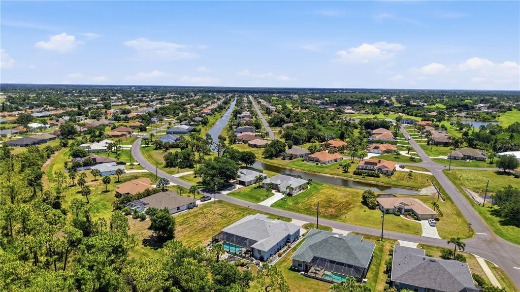 An aerial view shows a suburban neighborhood with houses, a canal, and surrounding green space — 143 LONG MEADOW LANE, ROTONDA WEST, FL