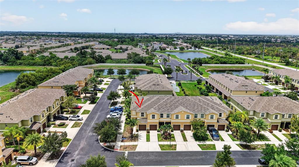 A two-story townhouse with a tan stucco exterior, two garage doors, and a palm tree — 1702 IVORY GOOSE PLACE, RUSKIN, FL