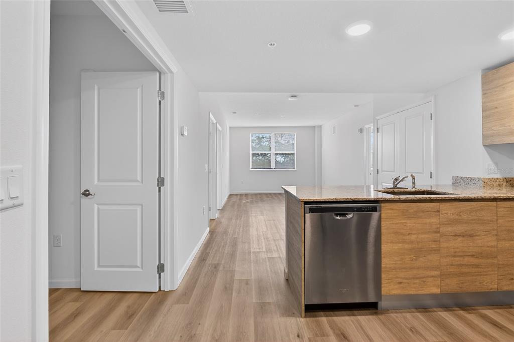 A kitchen island with a stainless steel dishwasher faces a hallway with light wood flooring — 1230 SOUTHSTATION PLACE UNIT 312, ORLANDO, FL