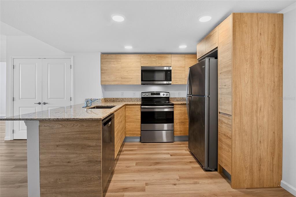 A modern kitchen features light wood cabinets, stainless steel appliances, and a granite countertop island — 1230 SOUTHSTATION PLACE UNIT 312, ORLANDO, FL
