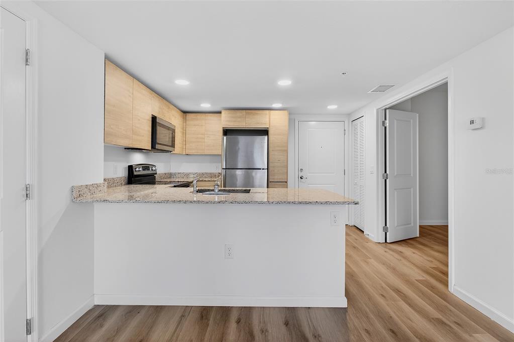 A kitchen with light wood cabinets, granite countertops, and stainless steel appliances overlooks a living area — 1230 SOUTHSTATION PLACE UNIT 312, ORLANDO, FL