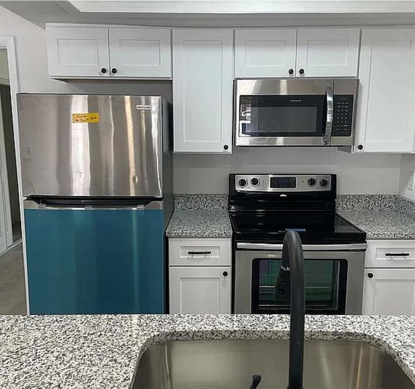 A kitchen features white cabinets, granite countertops, stainless steel appliances, and a blue-paneled refrigerator — 1227 WATERVIEW BOULEVARD W, LAKELAND, FL
