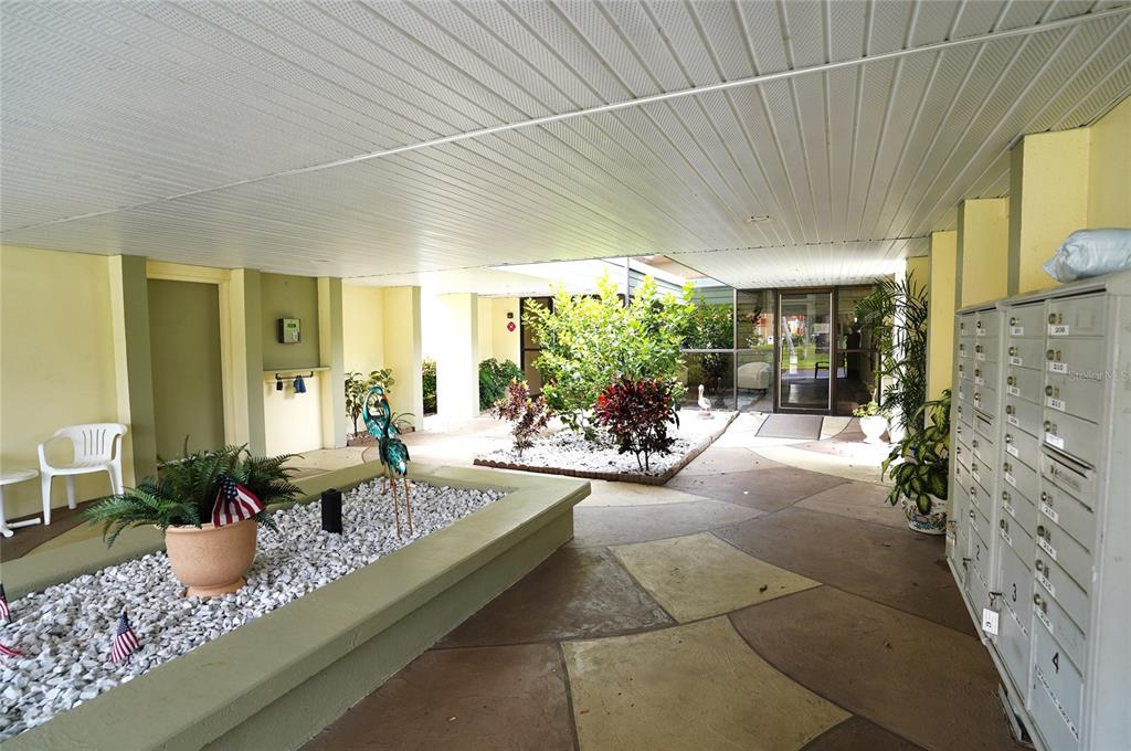 An outdoor covered entryway features a rock garden, potted plants, and a wall of mailboxes — 21267 GERTRUDE AVENUE UNIT 210, PORT CHARLOTTE, FL