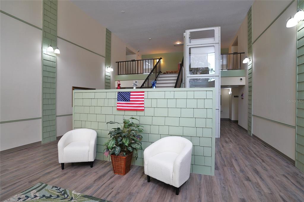A lobby features a green shingled wall, two white chairs, a plant, and an elevator — 21267 GERTRUDE AVENUE UNIT 210, PORT CHARLOTTE, FL