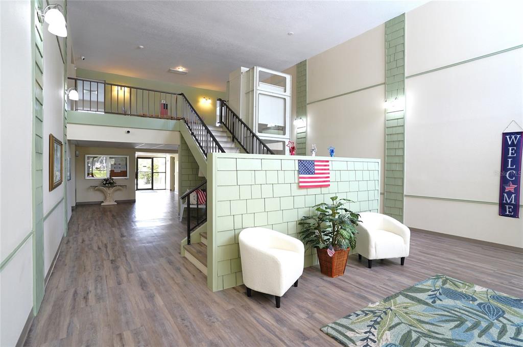 A bright lobby features a staircase, a wheelchair lift, two white chairs, and wood flooring — 21267 GERTRUDE AVENUE UNIT 210, PORT CHARLOTTE, FL