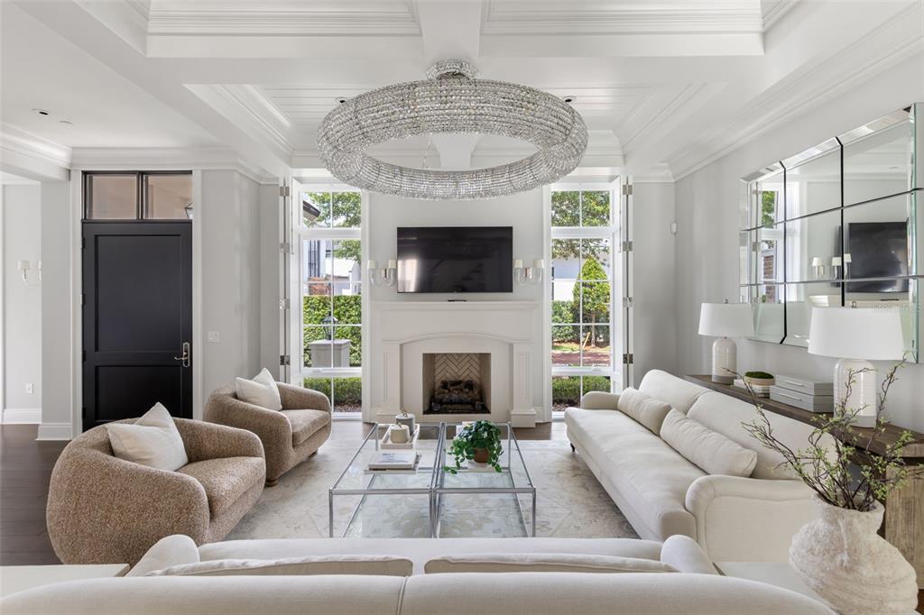 A bright living room features a crystal chandelier, fireplace, white sofa, and two armchairs — 649 N PARK AVENUE, WINTER PARK, FL