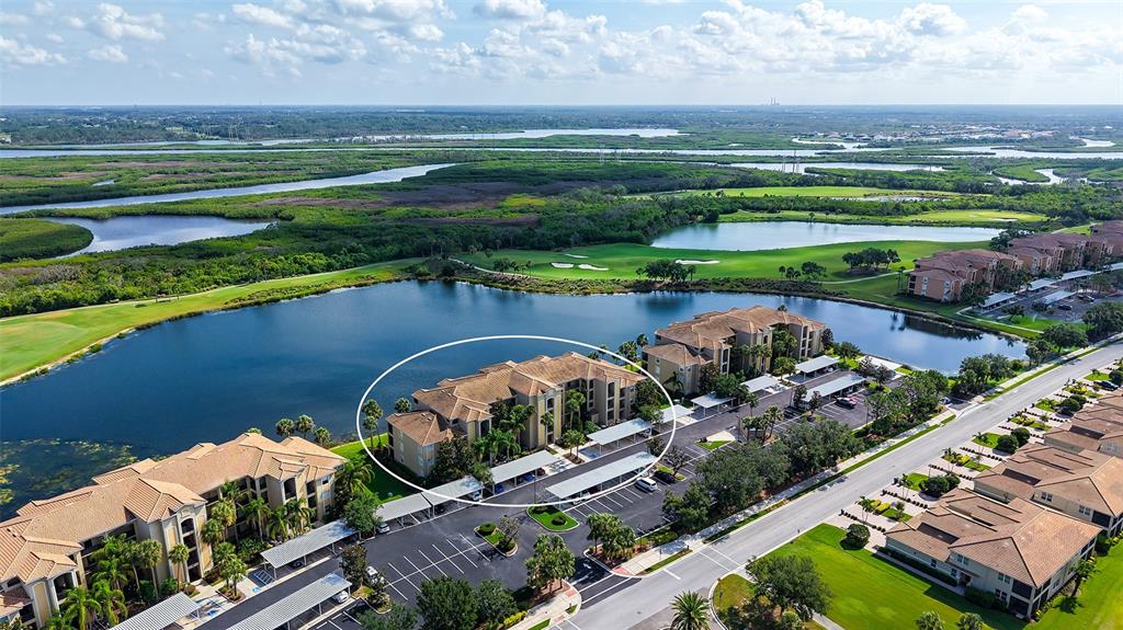 An aerial view shows a multi-story apartment building circled near a lake and golf course — 7803 GRAND ESTUARY TRAIL UNIT 307, BRADENTON, FL