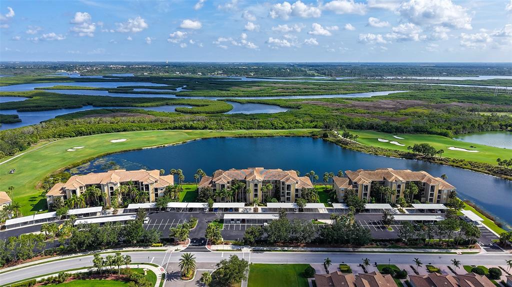 An aerial view shows three multi-story apartment buildings situated beside a lake and golf course — 7803 GRAND ESTUARY TRAIL UNIT 307, BRADENTON, FL