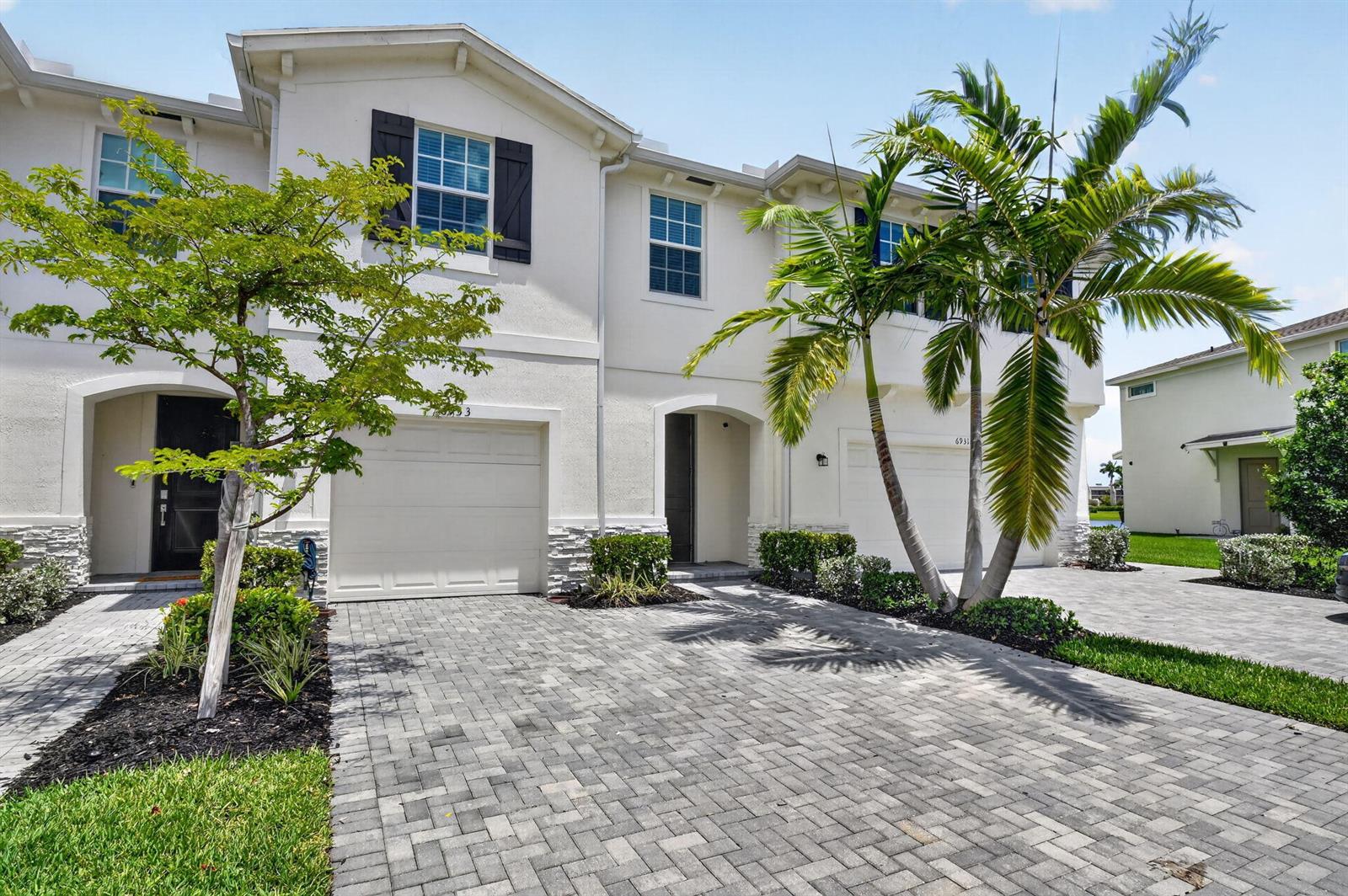 A two-story townhouse exterior with a paver driveway, white stucco walls, and palm trees — 6933 N Harbours Edge Avenue, Lake Worth FL 33467, LAKE WORTH, FL