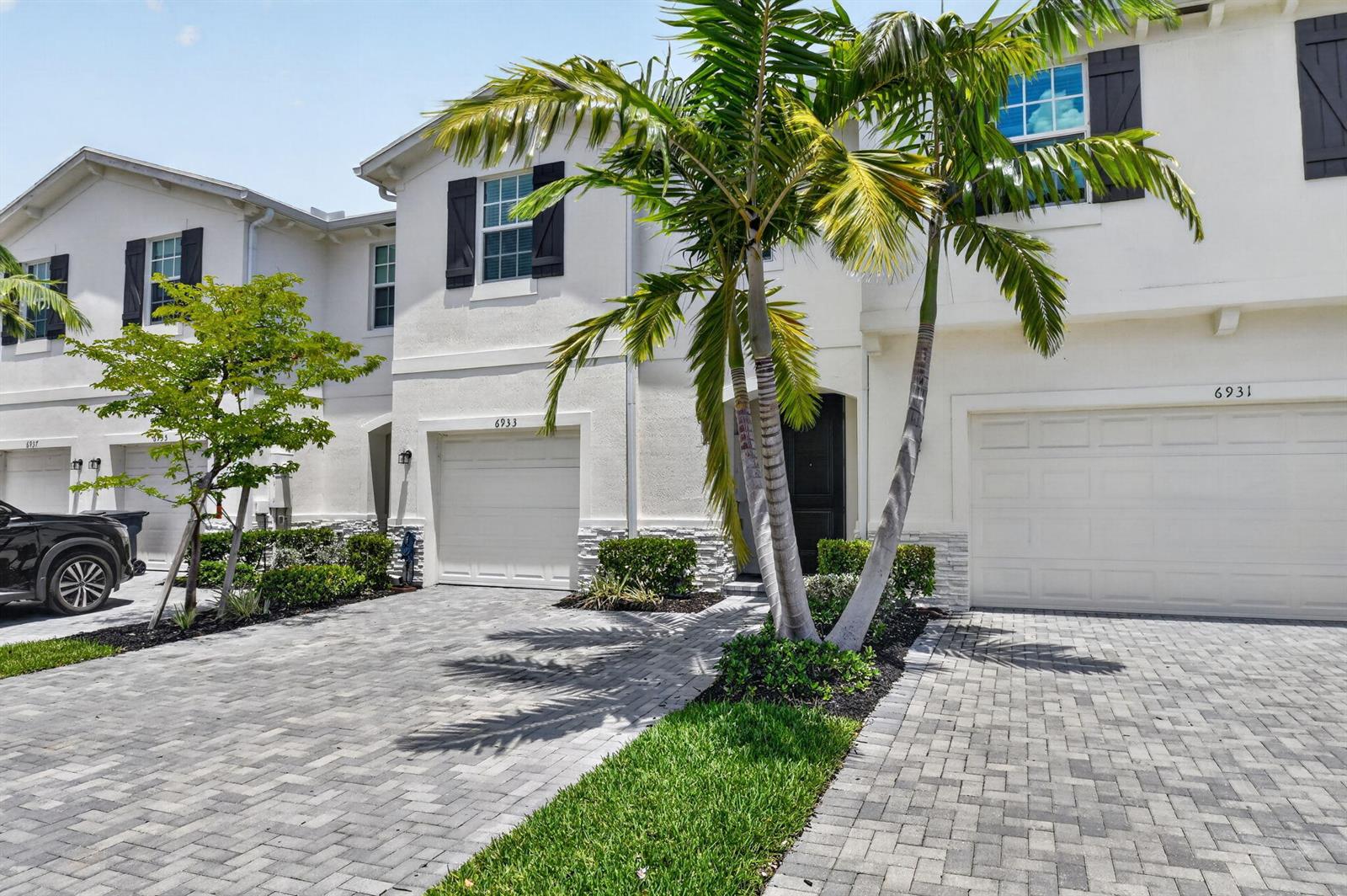 A paved driveway leads to the garages of two white townhouses with palm trees — 6933 N Harbours Edge Avenue, Lake Worth FL 33467, LAKE WORTH, FL