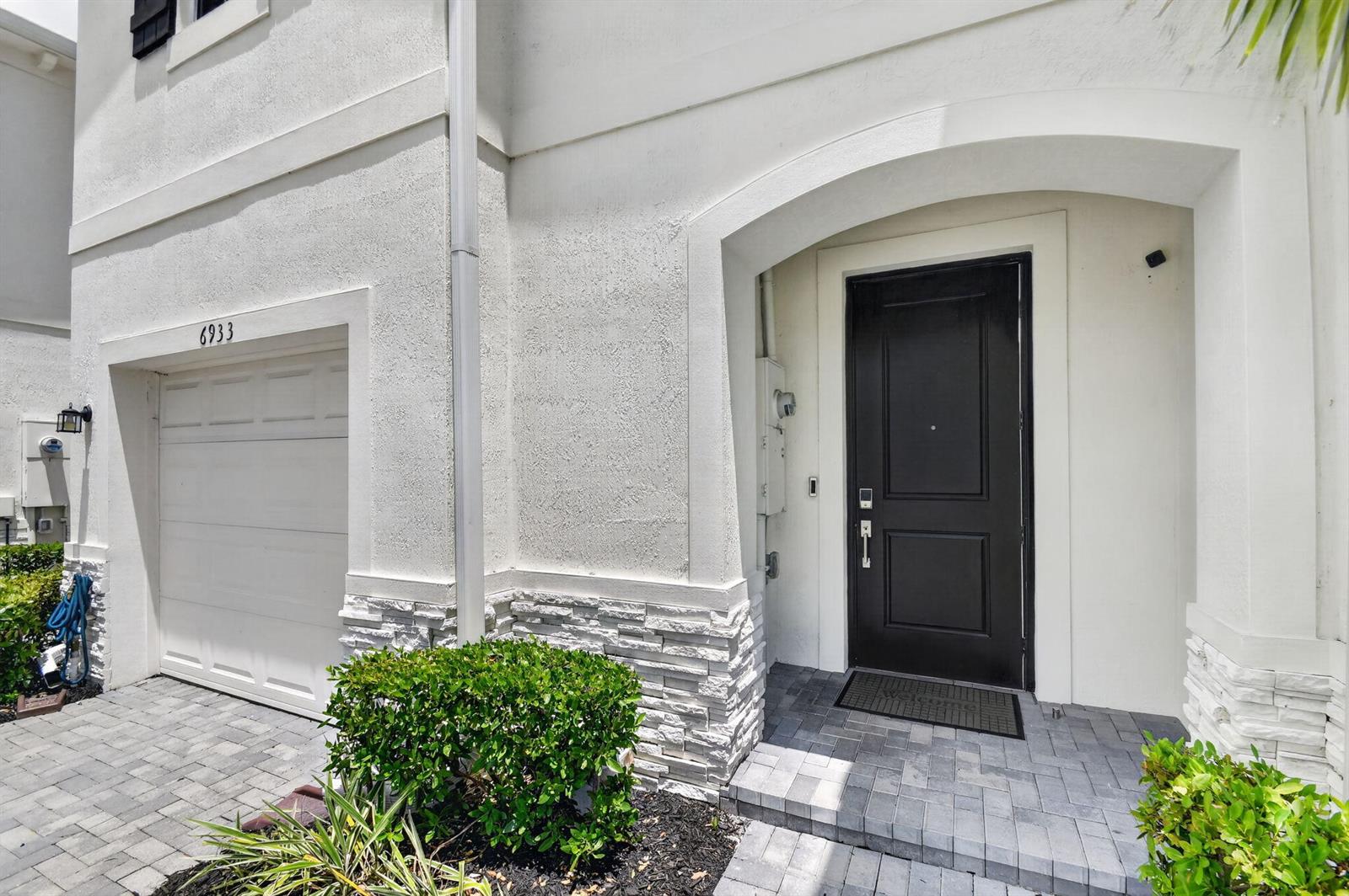 The exterior of a white stucco house features a black front door and garage — 6933 N Harbours Edge Avenue, Lake Worth FL 33467, LAKE WORTH, FL