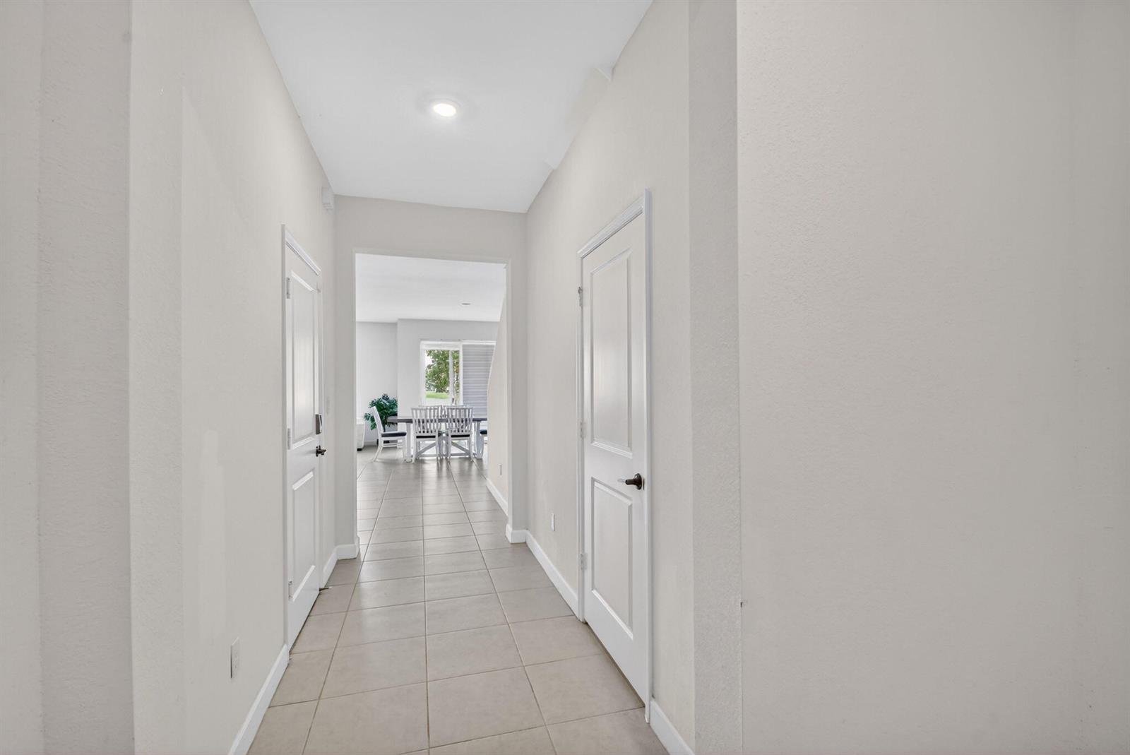 A hallway with light-colored tile flooring leads to a dining area with a sliding door — 6933 N Harbours Edge Avenue, Lake Worth FL 33467, LAKE WORTH, FL