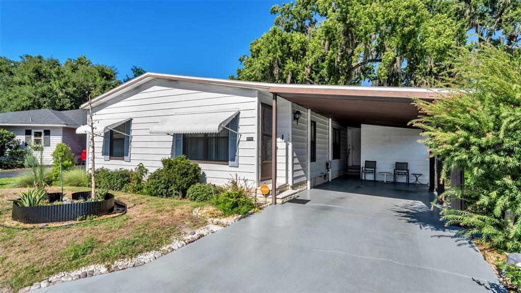 A single-story white house with a carport, metal awnings, and a landscaped front yard — 4959 COLONNADES CIRCLE W, LAKELAND, FL