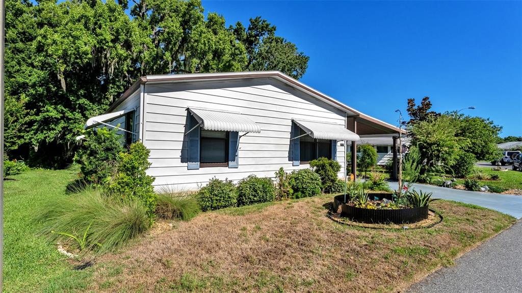 The exterior of a single-story home features white horizontal siding and metal window awnings — 4959 COLONNADES CIRCLE W, LAKELAND, FL