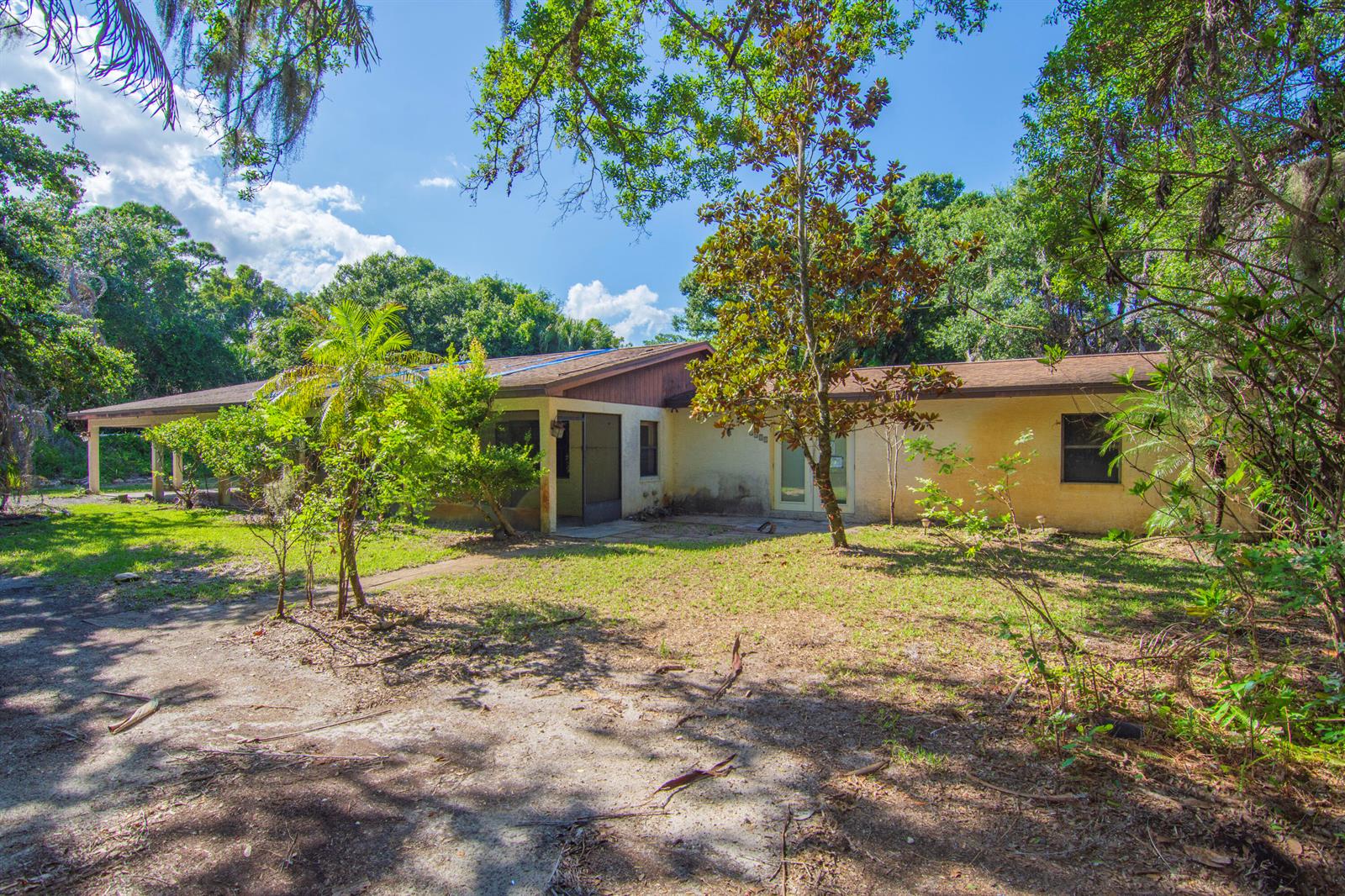 A single-story house with a covered porch and stucco exterior sits in a wooded yard — 1408 Russell Lane, Fort Pierce FL 34982, FORT PIERCE, FL