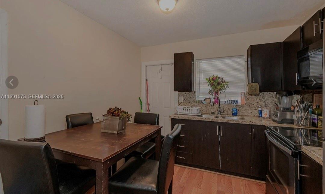 A kitchen features dark wood cabinets, granite countertops, and an adjacent wooden dining table — 110 NW 32nd Ave, Lauderhill FL 33311, LAUDERHILL, FL