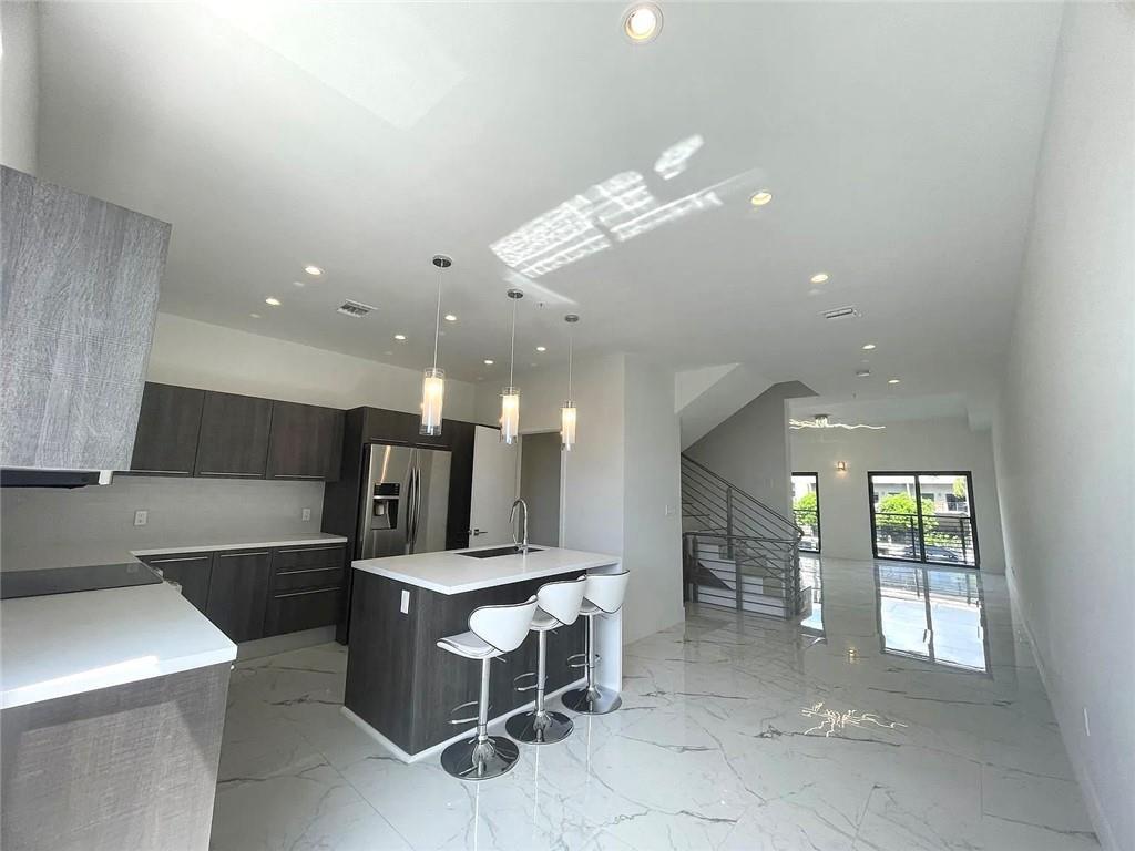 A modern kitchen features dark wood cabinetry, a white island with bar seating, and marble flooring — 113 SE 1st Circle, Pompano Beach FL 33060, POMPANO BEACH, FL