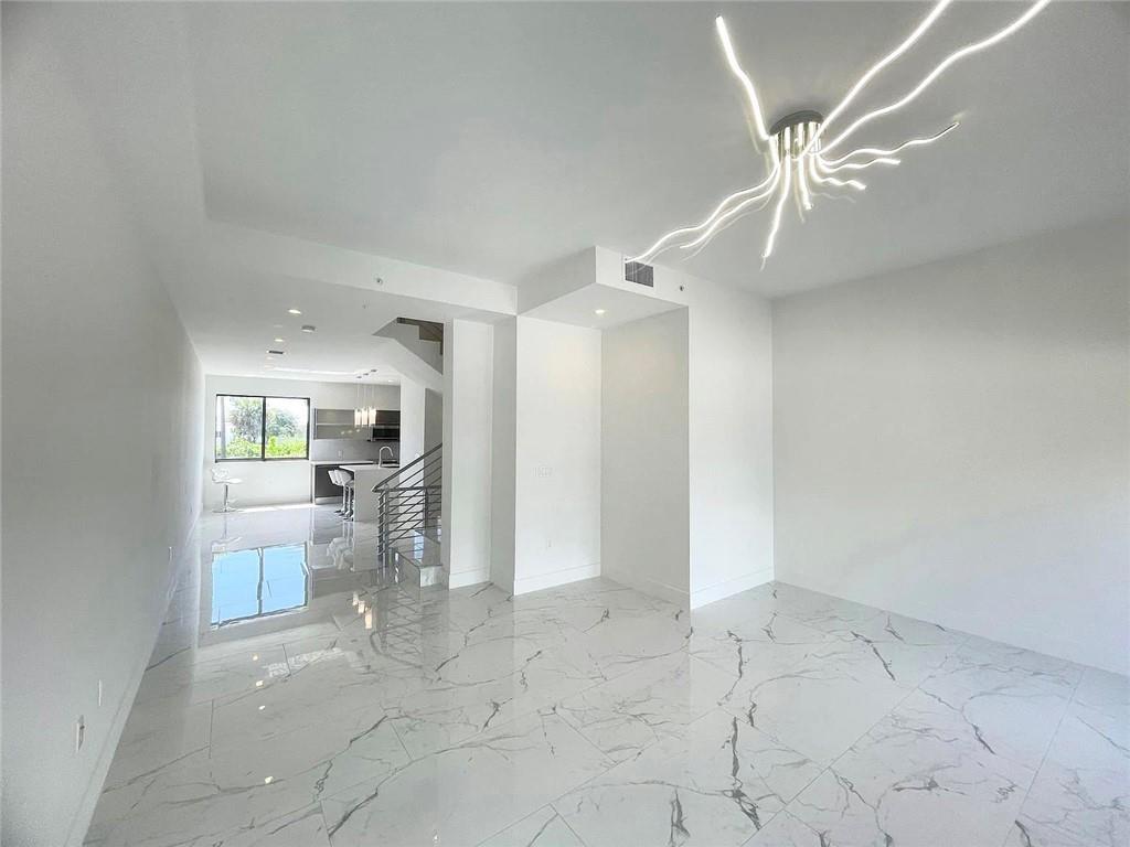 A bright, open-concept room features white marble-patterned tile flooring and a modern, abstract light fixture — 113 SE 1st Circle, Pompano Beach FL 33060, POMPANO BEACH, FL