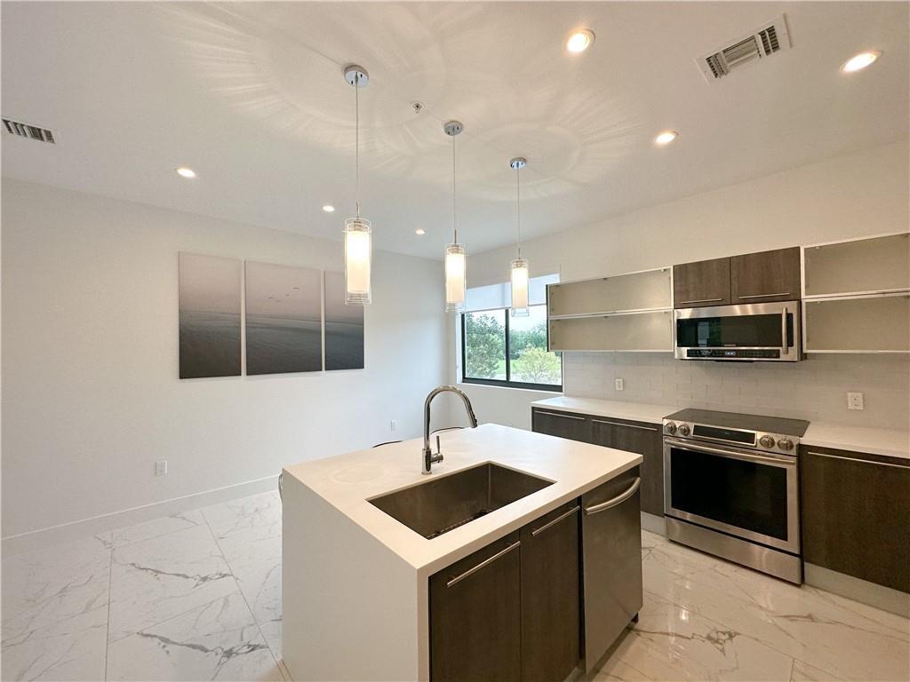 A modern kitchen features a white island with a sink, stainless appliances, and marble flooring — 113 SE 1st Circle, Pompano Beach FL 33060, POMPANO BEACH, FL