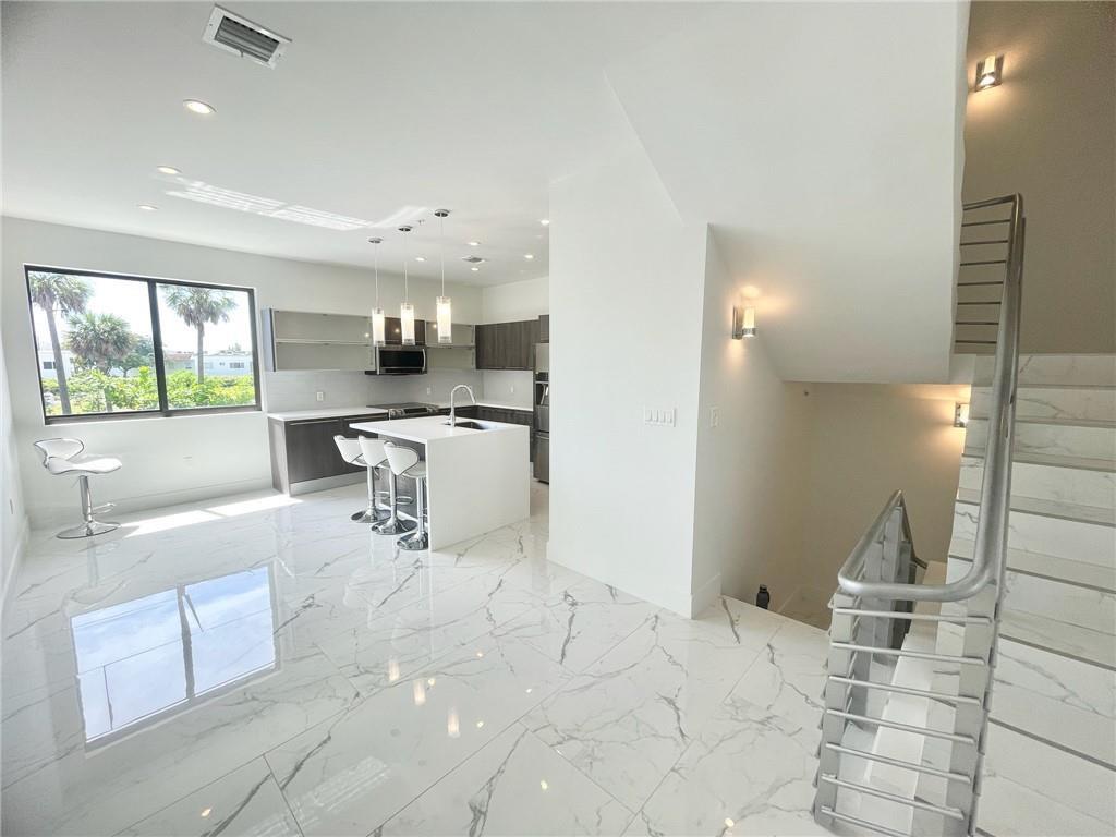 A modern kitchen features white marble floors, a center island, and a staircase with railings — 113 SE 1st Circle, Pompano Beach FL 33060, POMPANO BEACH, FL