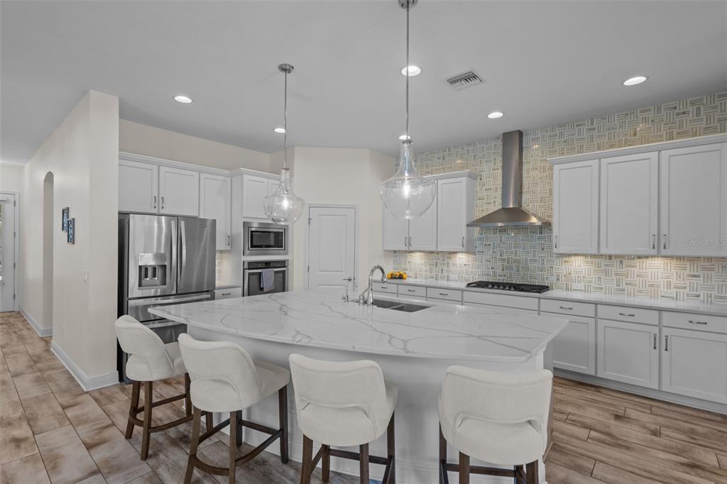 A modern kitchen features white cabinetry, a large marble-topped island, and a patterned tile backsplash — 2515 PORTICO STREET, ODESSA, FL