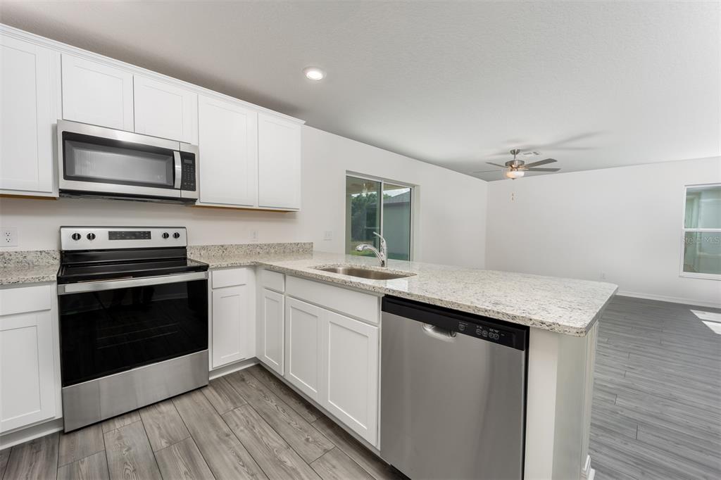 A kitchen with white cabinets, stainless steel appliances, and granite countertops overlooking a living area — 3208 SEVILLE STREET, LAKE ALFRED, FL