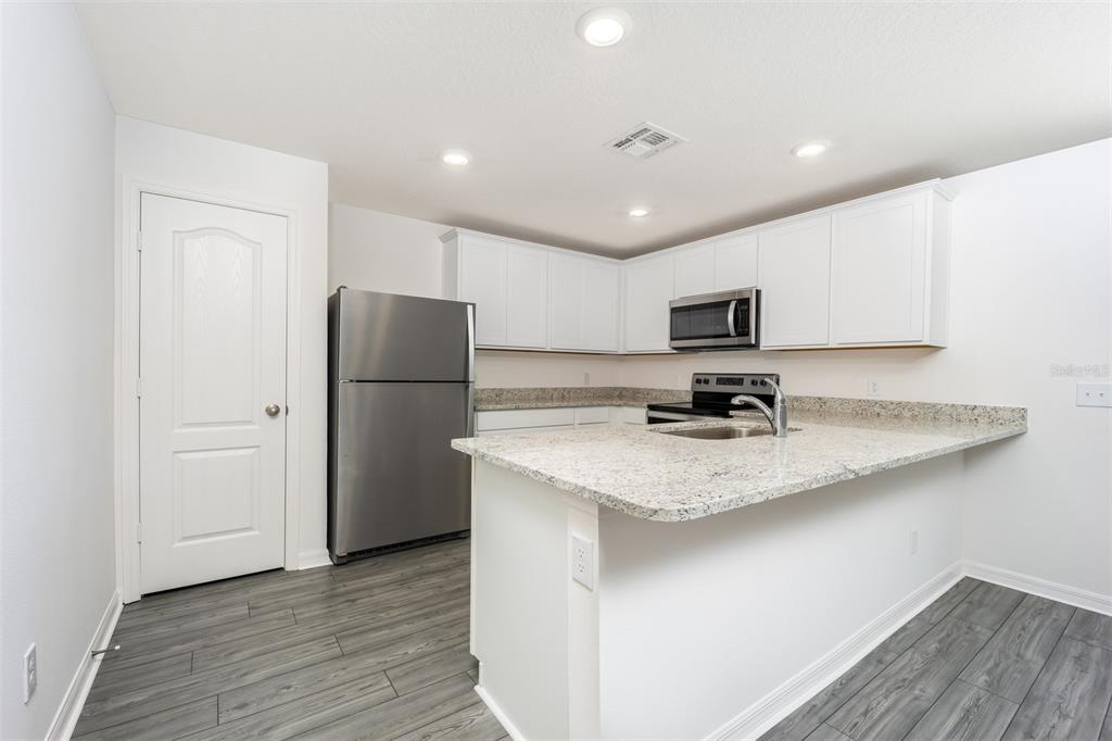 A kitchen with white cabinets, granite countertops, stainless steel appliances, and gray wood-look flooring — 3208 SEVILLE STREET, LAKE ALFRED, FL