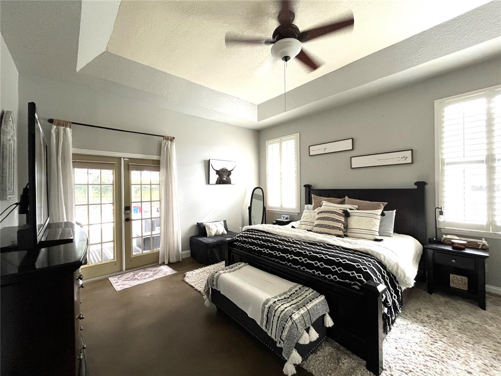 A bedroom features a dark wood bed frame, a ceiling fan, and glass patio doors — 10839 LANTANA CREST, CLERMONT, FL
