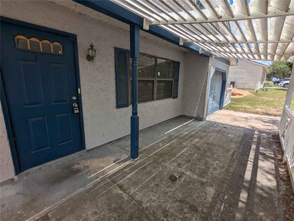 A concrete porch features a blue front door, a wooden pergola, and a garage entrance — 32 PALM RUN, OCALA, FL