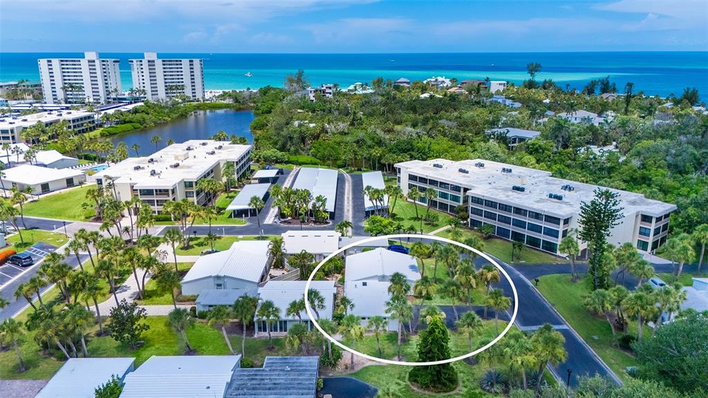 An aerial view shows a white residential building surrounded by palm trees and landscaping — 208 HOURGLASS WAY UNIT V11, SARASOTA, FL
