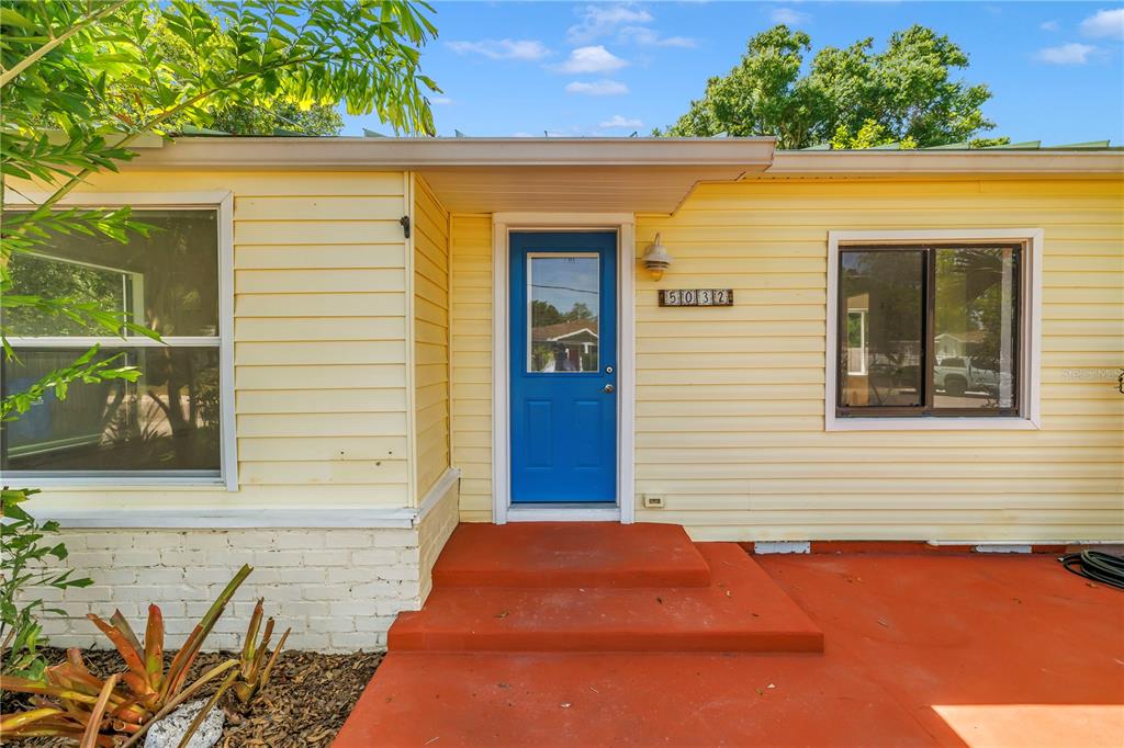 A yellow house exterior features a bright blue front door and a red concrete porch — 5032 19TH STREET N, ST PETERSBURG, FL