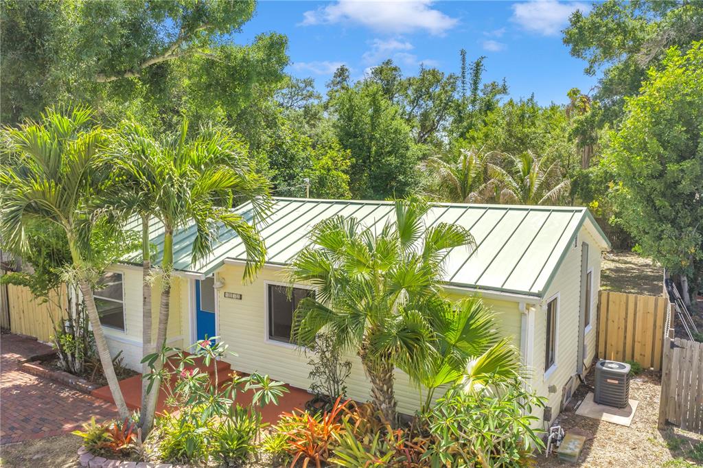 A yellow house with a green metal roof surrounded by palm trees and lush landscaping — 5032 19TH STREET N, ST PETERSBURG, FL