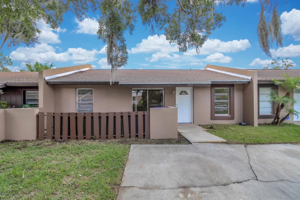A single-story townhouse exterior features a brown facade, a small fenced patio, and a driveway — 3143 STONECASTLE ROAD, ORLANDO, FL