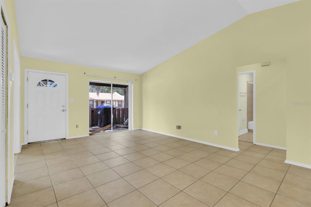 A living room with light yellow walls, beige tile flooring, a front door, and sliding doors — 3143 STONECASTLE ROAD, ORLANDO, FL
