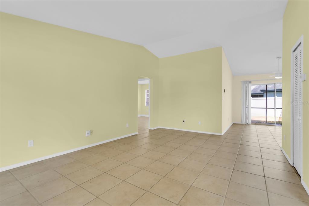 An empty living room with light yellow walls, tile flooring, and a sliding glass door — 3143 STONECASTLE ROAD, ORLANDO, FL