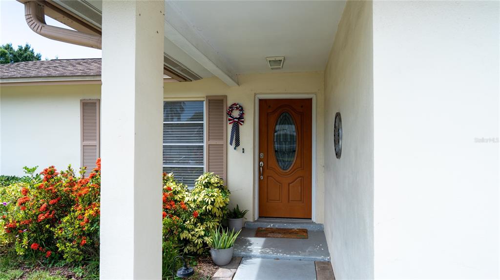 A covered entryway features a wooden front door with an oval glass insert and landscaping — 150 STAFFORD CIRCLE, PALM HARBOR, FL