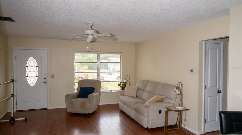 A living room features wood-look flooring, a beige sofa, an armchair, and a ceiling fan — 150 STAFFORD CIRCLE, PALM HARBOR, FL