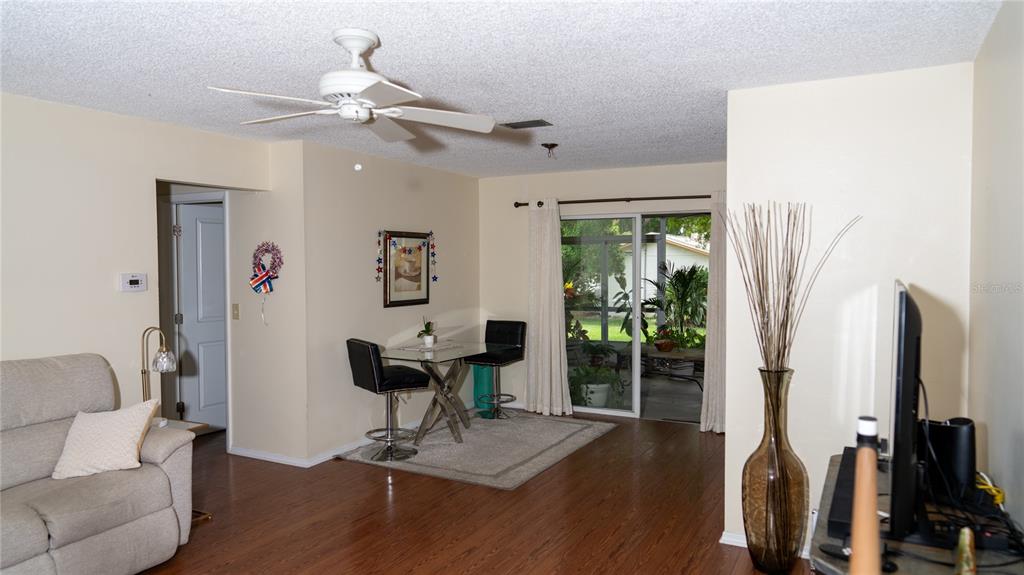 A living room with wood-look flooring, a ceiling fan, a dining area, and sliding glass doors — 150 STAFFORD CIRCLE, PALM HARBOR, FL