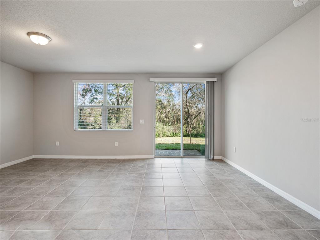 An empty room features gray tile flooring, light gray walls, a window, and sliding glass doors — 658 LEGACY LOOP, DAVENPORT, FL