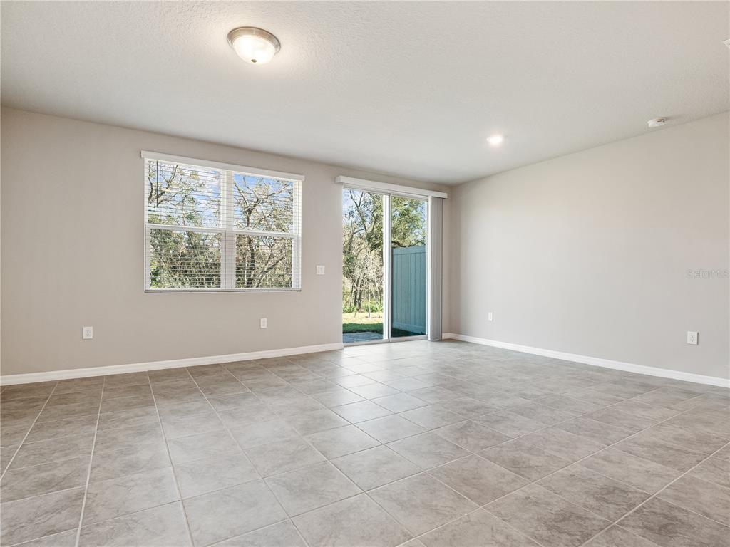 An empty room with light gray walls, tile flooring, a window, and sliding glass doors — 658 LEGACY LOOP, DAVENPORT, FL