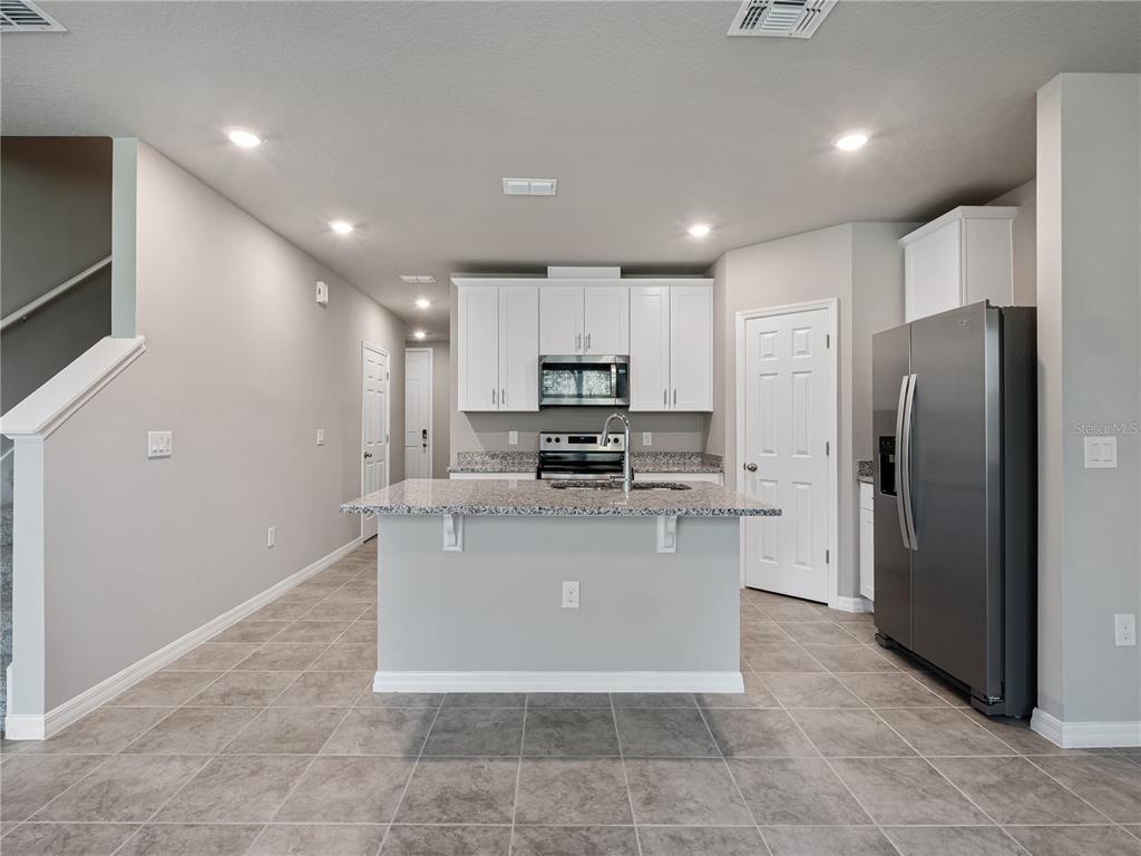 A kitchen features white cabinets, granite countertops, a center island, and stainless steel appliances — 658 LEGACY LOOP, DAVENPORT, FL