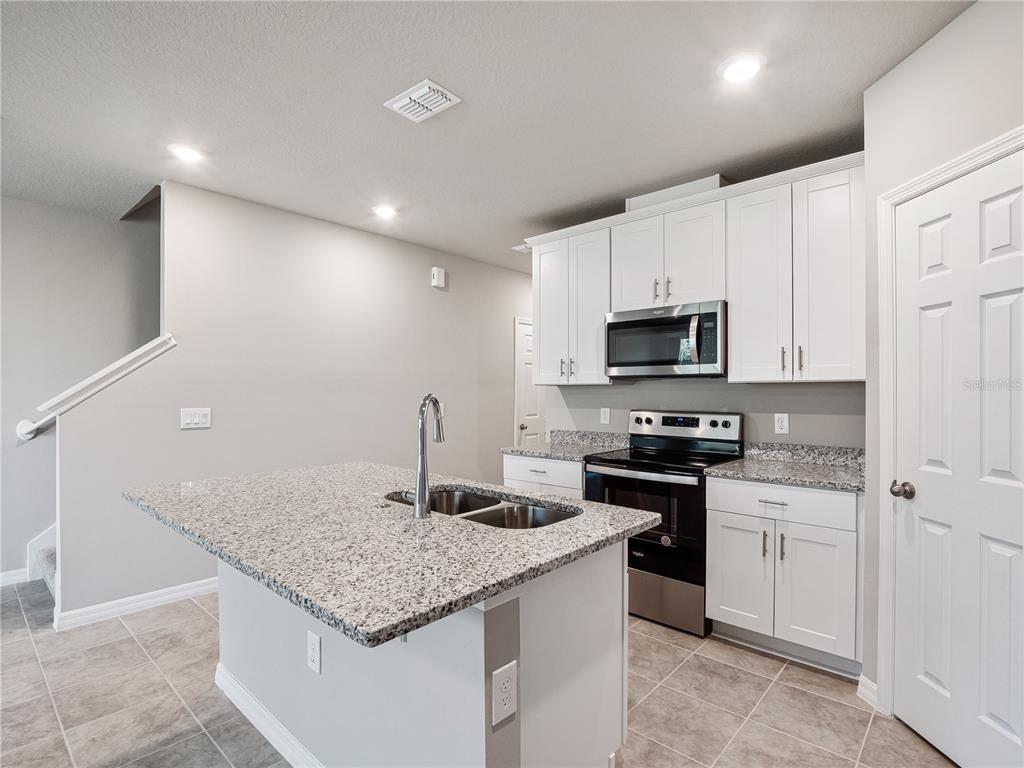 A kitchen with white cabinets, granite countertops, a center island, and stainless steel appliances — 658 LEGACY LOOP, DAVENPORT, FL