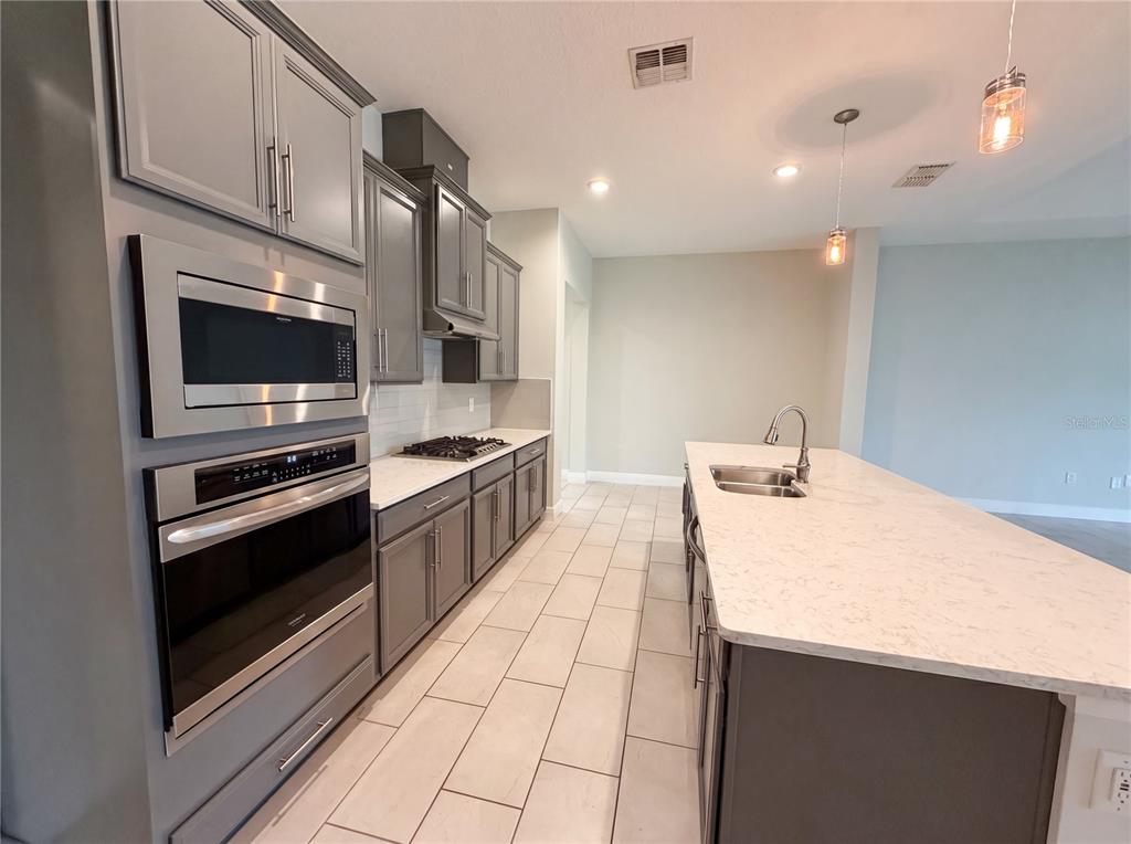 A modern kitchen features gray cabinets, stainless steel appliances, and a large white quartz island — 432 NOWELL LOOP, DELAND, FL