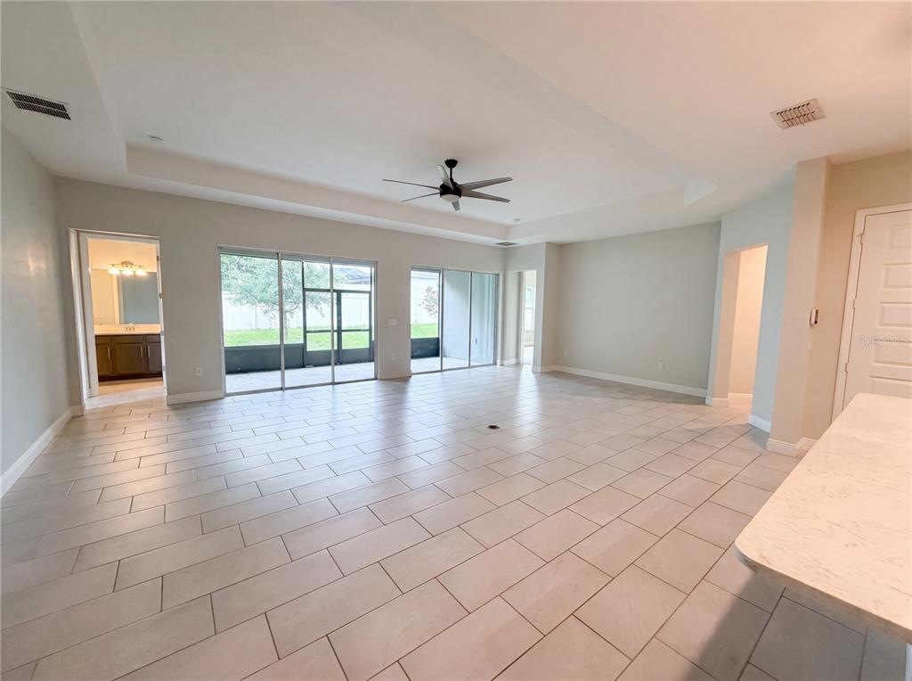 A spacious living area features light tile flooring, a tray ceiling with a fan, and sliding doors — 432 NOWELL LOOP, DELAND, FL