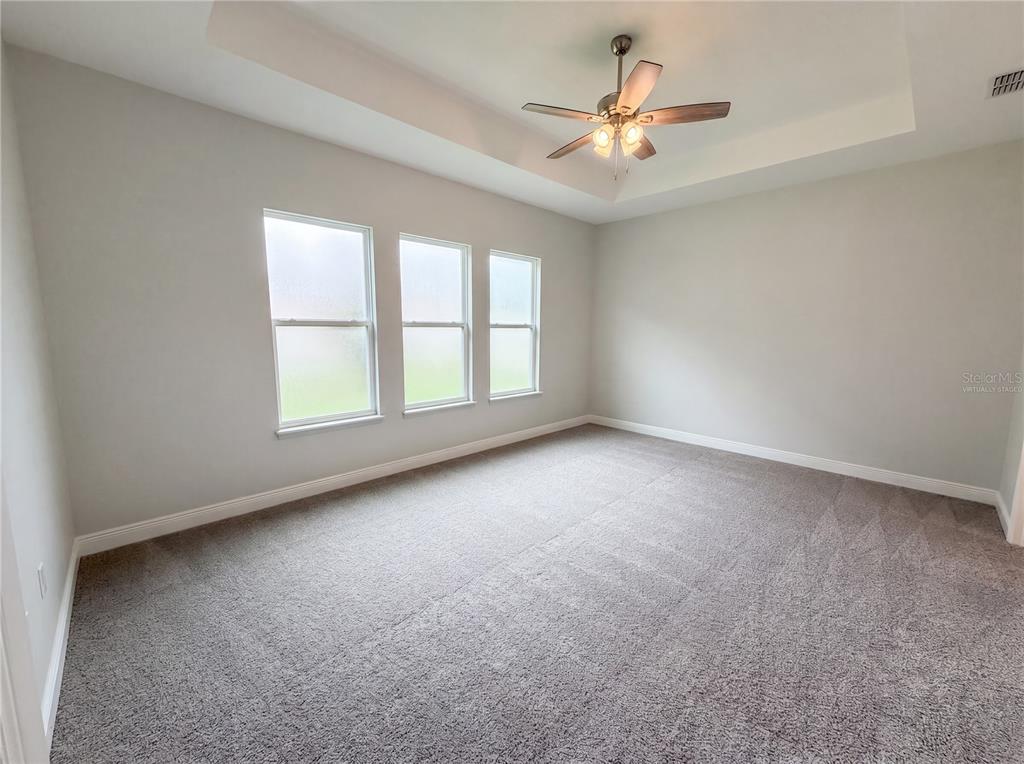 An empty bedroom features gray carpet, light walls, a tray ceiling, and a ceiling fan — 432 NOWELL LOOP, DELAND, FL